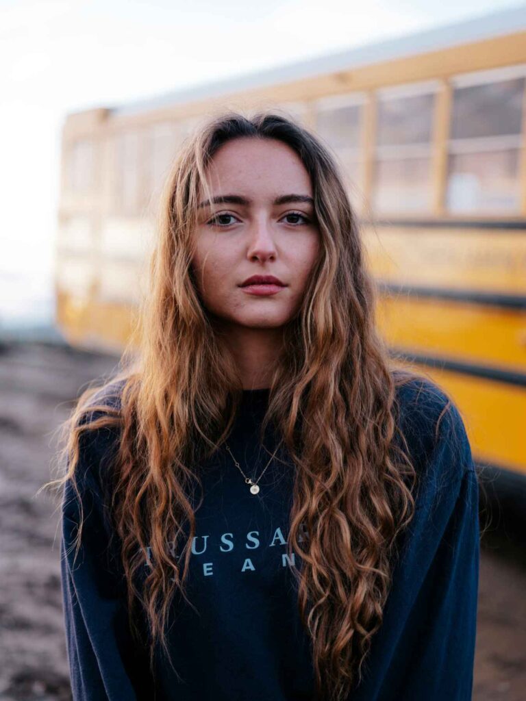 A High School-aged girl in front of a school bus.